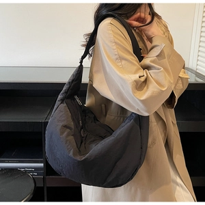 Detail view of a large black padded nylon crossbody bag with adjustable wide strap on model