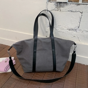 Détail d'un grand sac cabas en toile grise avec anses en cuir noir sur un sol en bois