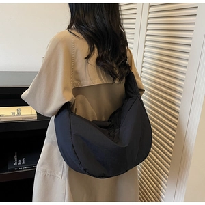 Detail showing the black crescent nylon crossbody bag worn on shoulder by a model