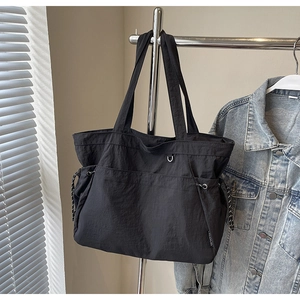 Détail du sac cabas en nylon noir avec cordons de serrage latéraux et étiquette tissée