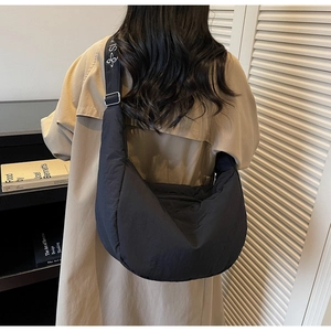 Detail of black quilted crescent bag featuring wide shoulder strap with artistic logo