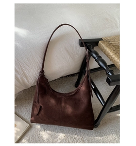 Detailed view of brown suede hobo bag with fringe decoration on white rug