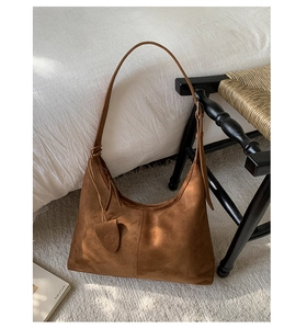Detail of a brown suede hobo tote bag with a heart charm on a grey rug background