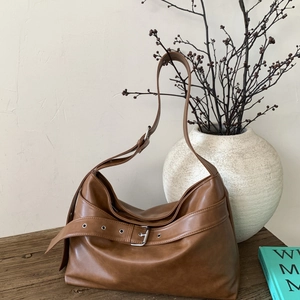 Vintage brown leather hobo shoulder bag with metal buckle on a rustic wooden table