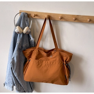 Vue détaillée du sac cabas en nylon orange accroché sur un cintre en bois avec veste en jean