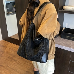 Detail of a large black leopard print tote bag shown on a model in a cozy indoor setting