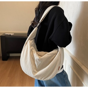 Close-up of a beige quilted dumpling crossbody bag with a wide strap on a model