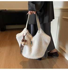 Détail d'un sac cabas en fausse fourrure blanche avec anses en cuir et breloque ours