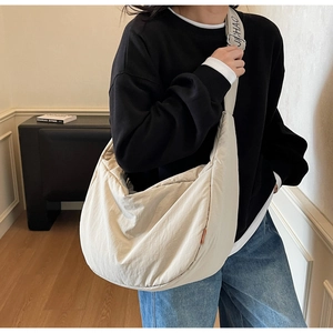 Detail of a large beige nylon crossbody bag featuring an adjustable letter print strap