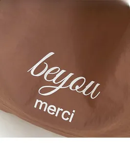 Detail of a brown tote bag featuring white printed beyou and merci text slogans