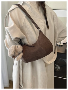 Dark brown suede hobo bag with plush rabbit charm worn by model in beige trench coat