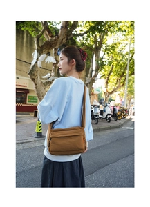Detailed view of deep brown nylon crossbody bag with side orange label on casual strap