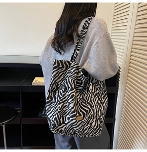 Detail of a large zebra pattern tote bag with a metal handmade tag worn on shoulder