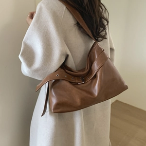 Detail view of brown leather shoulder bag with decorative buckle and silver eyelets