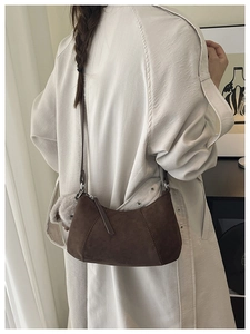 Detail einer braunen Wildleder-Handtasche mit grauem Pelzanhänger an einem Model