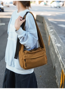 Outdoor shot of a brown large capacity nylon crossbody messenger bag on a striped sweater
