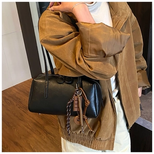 Detail of a black oil-wax leather shoulder bag featuring a unique multi-element pendant charm