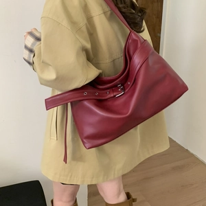 Close-up of a burgundy leather tote with metallic buckles on a khaki trench coat