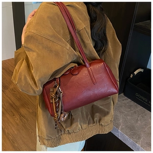 Detail view of burgundy leather shoulder bag with glossy texture and woven rope accents
