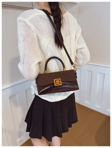 Detail der dunkelbraunen Handtasche mit Materialmix und Goldschnalle am Modell