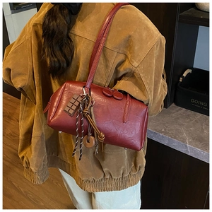 Detailed side view of a vintage burgundy cylindrical shoulder bag with creative charms