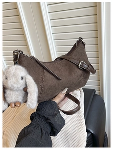 Detail einer dunkelbraunen Wildleder-Beuteltasche mit einem weißen Plüschhasen-Anhänger