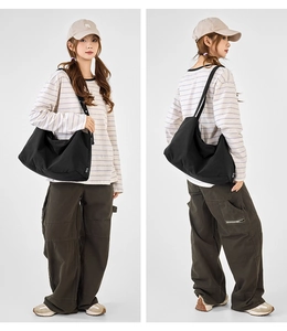 Detail of a large black canvas tote bag with drawstring folds and white brand label