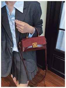 Nahaufnahme der weinroten Handtasche mit goldener Schnalle an einem Model in Grau
