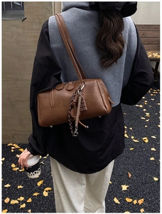 Close-up of vintage brown leather cylinder shoulder bag with creative charms and autumn style
