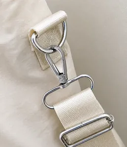 Dettaglio del gancio in metallo argento e tracolla in nylon beige della borsa