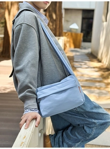 Detail of light blue nylon crossbody bag with black adjustable strap in outdoor natural light