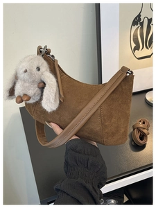 Detail einer braunen Hobo-Tasche aus Wildleder mit weißem Plüschhasen-Anhänger Accessoire