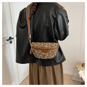 Detail view of leopard print crossbody bag with gold chain and wide strap on a model