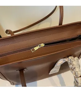 Detailed close-up of smooth metal zipper and silk scarf on a brown leather tote bag