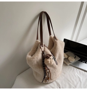 Gros plan d'un sac seau beige duveteux avec bandoulière en cuir et breloque ours