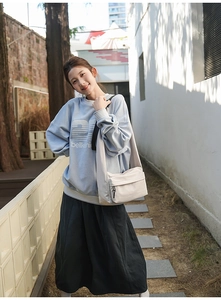 Detail of a large off-white nylon crossbody bag with a front zipper pocket and wide strap