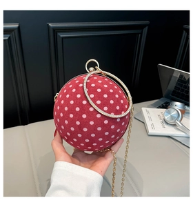Detail of red spherical evening bag with white polka dots and sparkling gold ring handle