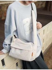 Close-up of a large capacity cream nylon crossbody bag with wide strap and orange label