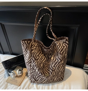 Detail of zebra-print plush tote bag featuring a gold handmade metal tag on soft fabric