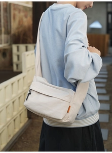 Close-up of a large beige nylon crossbody messenger bag with orange brand tag detail