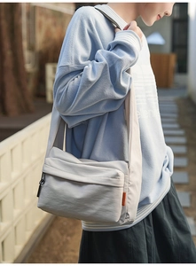 Detail of grey nylon crossbody bag with orange tag shown on a casual model outfit