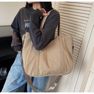 Detail van beige nylon draagtas met verstelbare riem gedragen door een vrouwelijk model