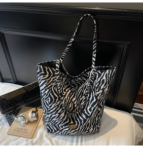 Zebra print tote bag with handmade metal logo on a bed with laptop and headphones