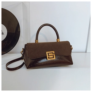 Detail einer dunkelbraunen Handtasche mit Wildlederklappe und goldenem Verschluss