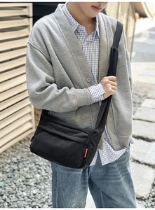 Detail of black nylon messenger bag featuring an orange woven label and wide shoulder strap