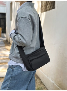 Detail of a black nylon crossbody bag shown in an urban street style casual outfit