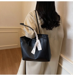 Minimalist black leather tote bag with checkerboard scarf detail on woman's shoulder