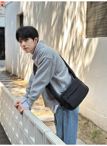 Outdoor street shot of a large black nylon crossbody bag worn with a casual gray jacket