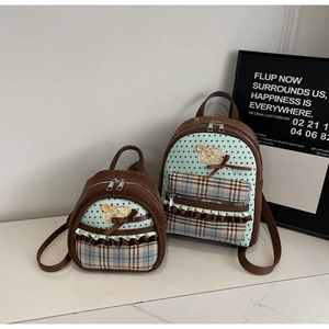 Detail of two mint green backpacks with star patterns, plaid pockets, and bow accents