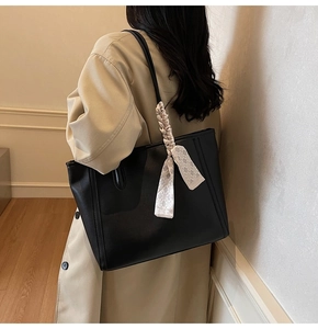 Detail view of black leather tote bag with a checkered silk scarf on the thin handle